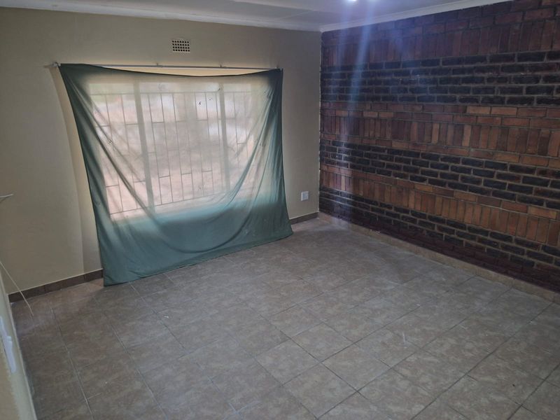 An empty living room featuring a prominent exposed brick wall, tiled flooring, and a window fitted with security bars.