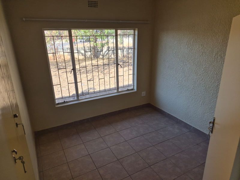 An empty bedroom featuring tiled flooring, textured walls, and a large window fitted with security bars.