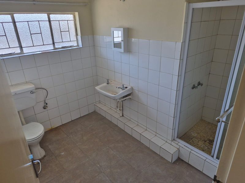 A dated bathroom featuring a shower enclosure, wall-mounted basin, and toilet, with tiled walls and flooring throughout.