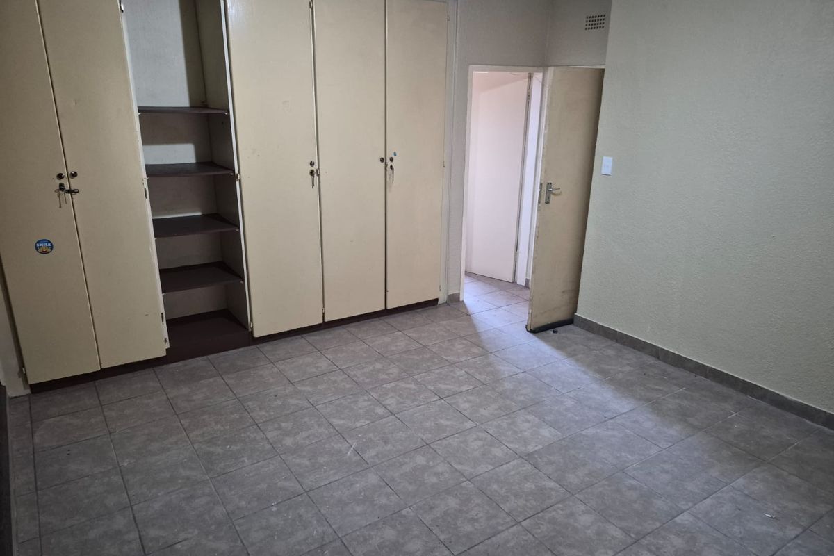 An empty bedroom featuring tiled flooring and built-in storage cupboards, offering a blank canvas for potential renovation or interior design updates.