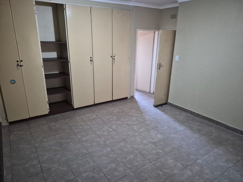 An empty bedroom featuring tiled flooring and built-in storage cupboards, offering a blank canvas for potential renovation or interior design updates.
