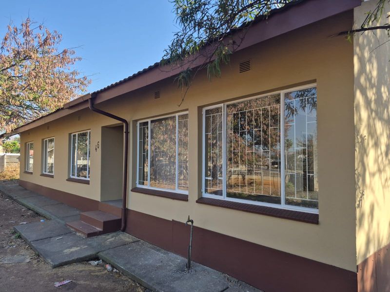 Front elevation of a single-story house featuring a painted facade, tiled roof, and security-barred windows with an adjacent concrete walkway.
