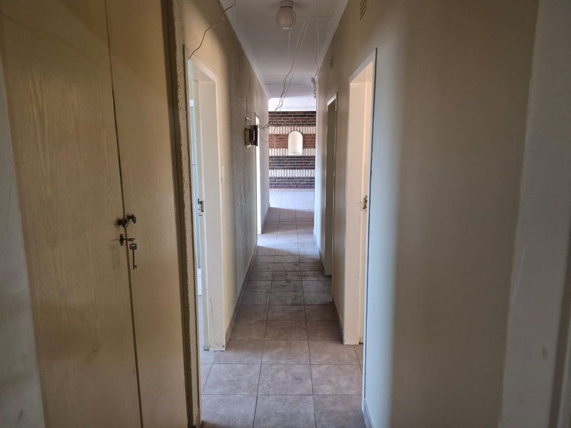 A long, empty hallway featuring tiled flooring and built-in storage cupboards, currently requiring cosmetic updates and electrical repairs.