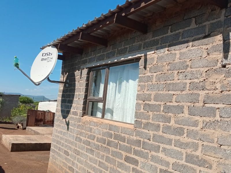Exterior view of a house featuring exposed concrete block walls, a corrugated metal roof, and an installed satellite dish.