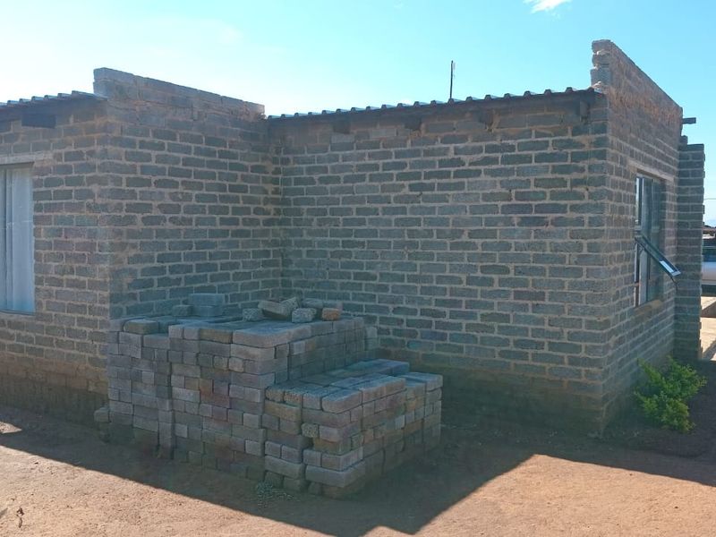 Rear view of a house under construction featuring exposed brick walls and corrugated metal roofing.