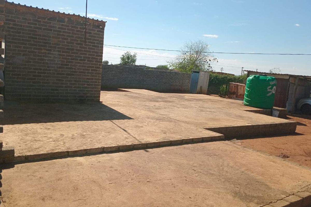 An outdoor rear area featuring a large concrete slab, unfinished brick walling, and a plastic water storage tank.