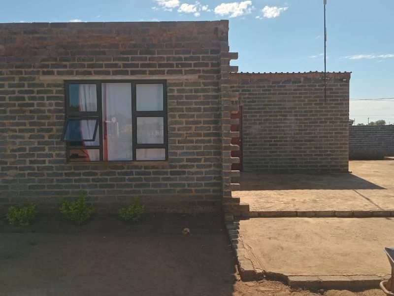 Front view of a single-story house featuring exposed brick construction, aluminium window frames, and an unfinished exterior ground area.
