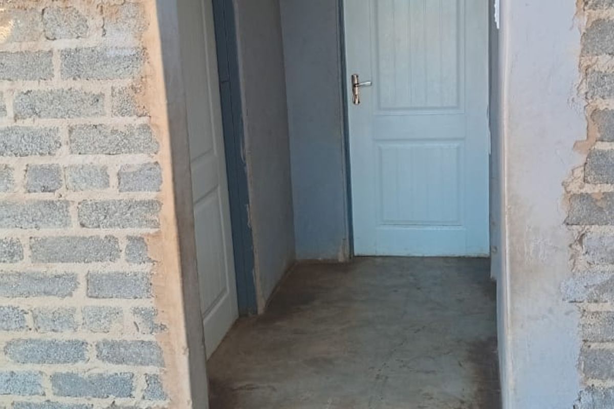A narrow hallway featuring unfinished exposed brick walls and concrete flooring, leading to internal doors.