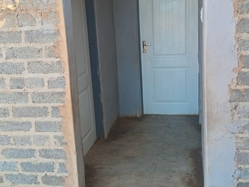 A narrow hallway featuring unfinished exposed brick walls and concrete flooring, leading to internal doors.