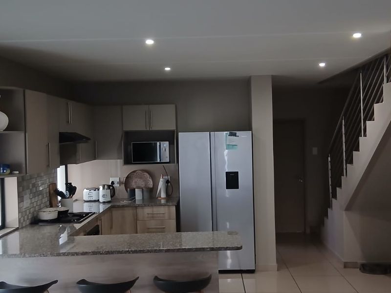 Modern open-plan kitchen featuring granite countertops, built-in cabinetry, and integrated appliances, seamlessly flowing into the living area with an adjacent staircase.