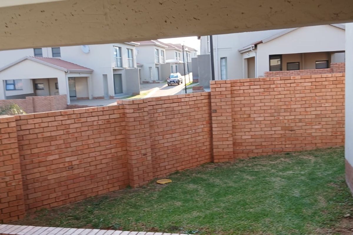 A view of the rear garden area featuring a face brick boundary wall and surrounding townhouse complex architecture.