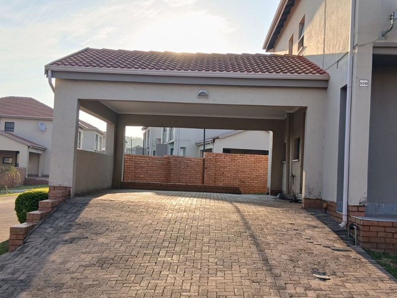 A spacious covered carport with a paved driveway and brick boundary wall, providing secure off-street parking for the townhouse.