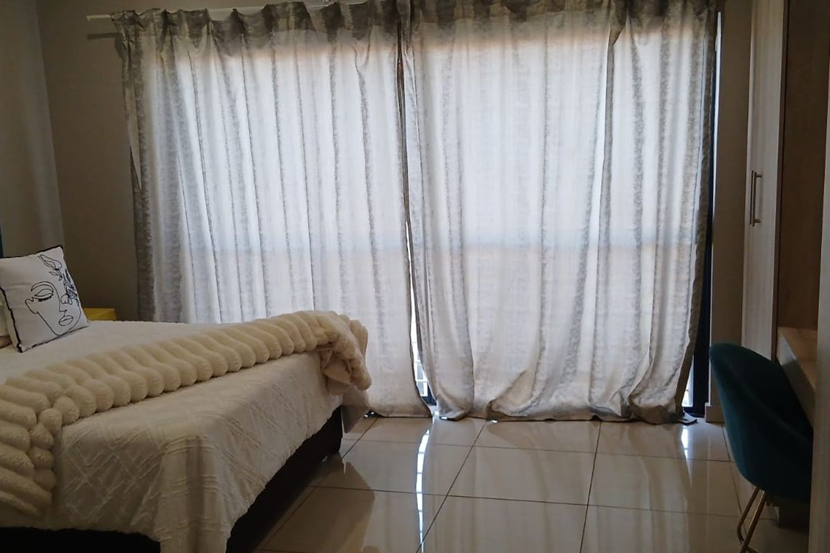 A well-lit bedroom featuring tiled flooring, built-in cupboards, and a large sliding glass door providing access to the exterior.