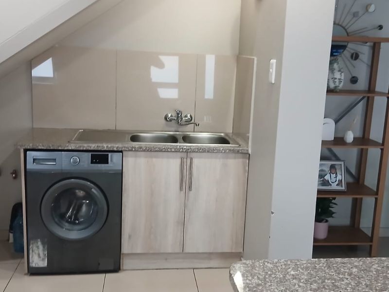Compact laundry area located under the staircase, featuring built-in cabinetry, a double sink, and tiled splashback.