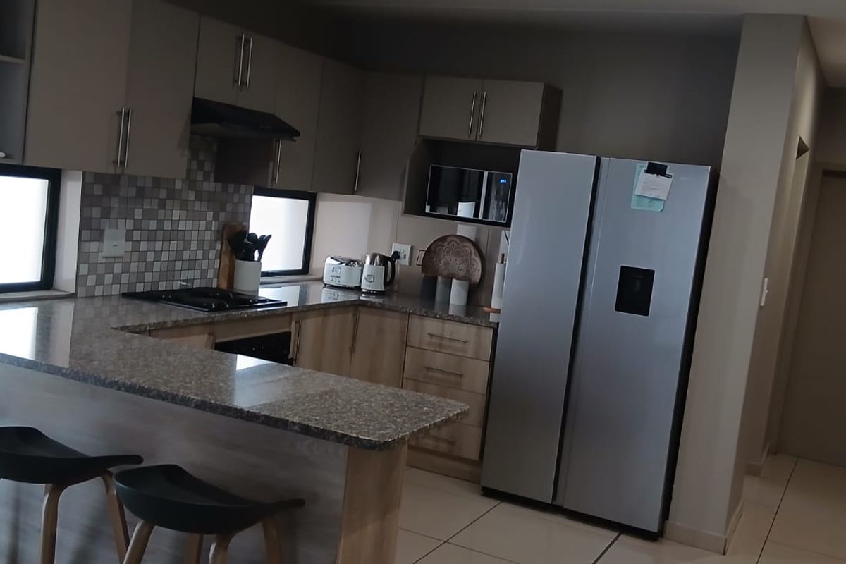 Modern kitchen featuring granite countertops, built-in cabinetry, a gas hob with extractor, and a breakfast bar, finished with neutral tiled flooring.