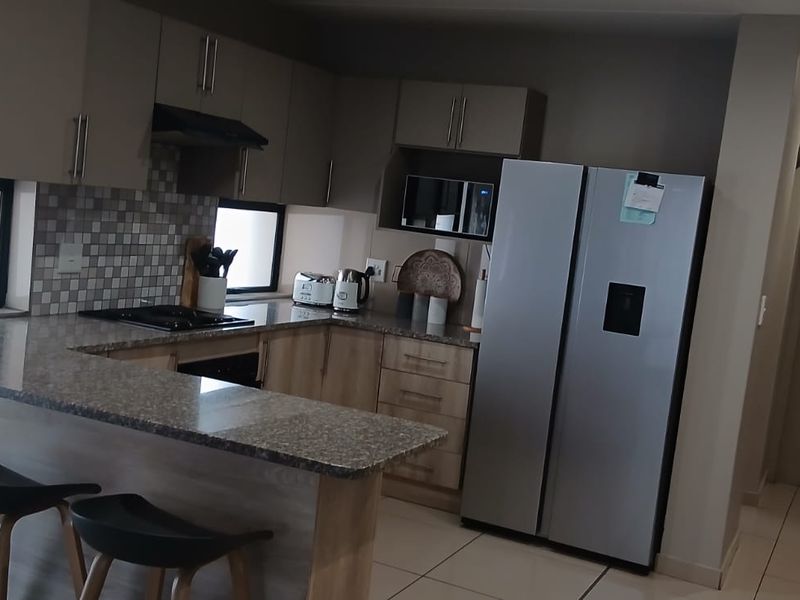 Modern kitchen featuring granite countertops, built-in cabinetry, a gas hob with extractor, and a breakfast bar, finished with neutral tiled flooring.