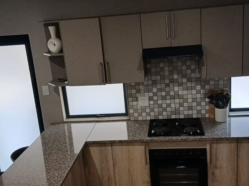 Modern kitchen featuring granite countertops, built-in cabinetry, mosaic tile backsplash, and integrated appliances including a gas hob and oven.