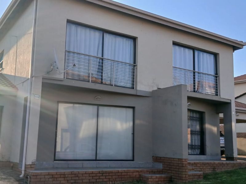 Front elevation of a double-story townhouse featuring a brick base, balcony with metal railings, and sliding door access.