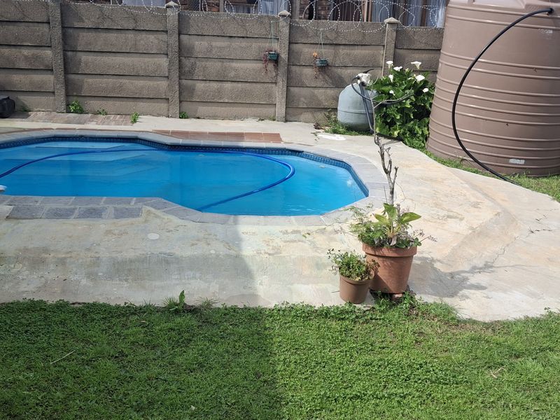 Outdoor pool area featuring a concrete surround, boundary wall with security fencing, and a water storage tank.