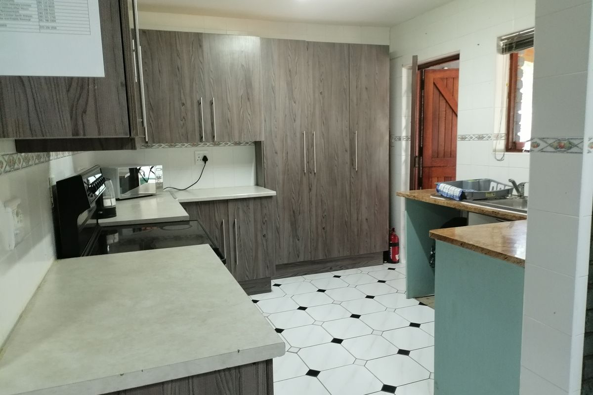Functional kitchen featuring wood-look cabinetry, laminate countertops, tiled flooring, and a double sink with a tiled backsplash.