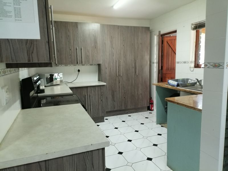 Functional kitchen featuring wood-look cabinetry, laminate countertops, tiled flooring, and a double sink with a tiled backsplash.