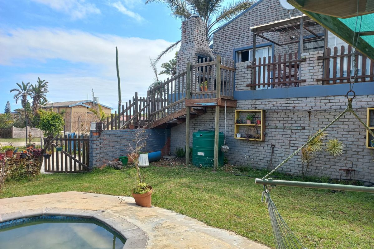 Rear exterior view featuring a brick house with an outdoor fireplace, wooden staircase, deck, and a swimming pool set in a garden area.