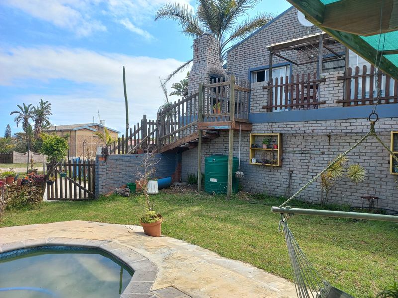 Rear exterior view featuring a brick house with an outdoor fireplace, wooden staircase, deck, and a swimming pool set in a garden area.