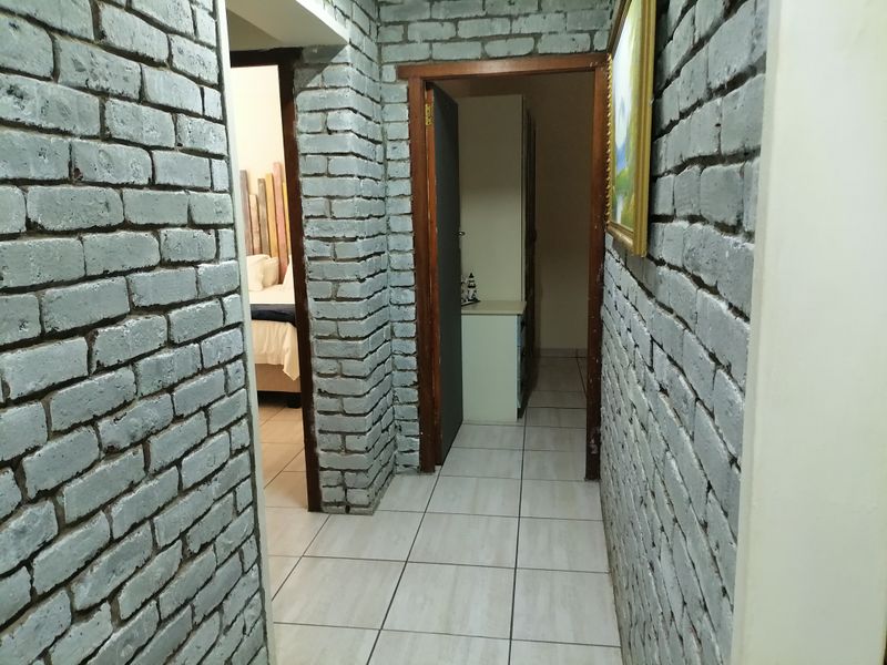 A hallway featuring exposed grey brick walls and light-colored ceramic floor tiles, providing access to adjacent rooms.