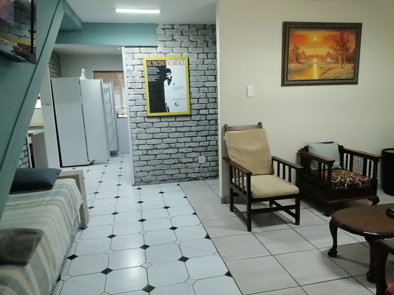 A living area featuring a brick veneer feature wall, ceramic tiled flooring, and an adjacent staircase leading to an upper level.