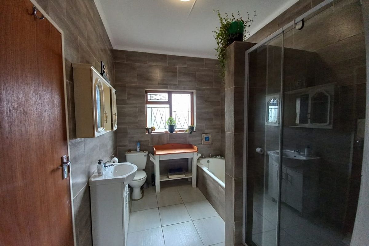 A functional bathroom featuring tiled walls and floors, a pedestal basin, a built-in bathtub, and a separate glass-enclosed shower.