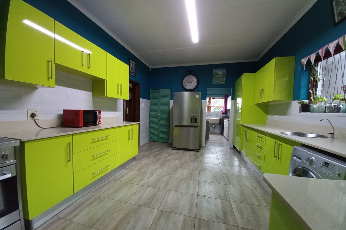 Spacious kitchen featuring vibrant lime green high-gloss cabinetry, stone countertops, tiled flooring, and integrated appliances with a functional layout.
