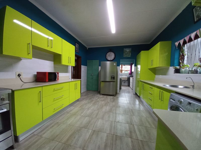 Spacious kitchen featuring vibrant lime green high-gloss cabinetry, stone countertops, tiled flooring, and integrated appliances with a functional layout.