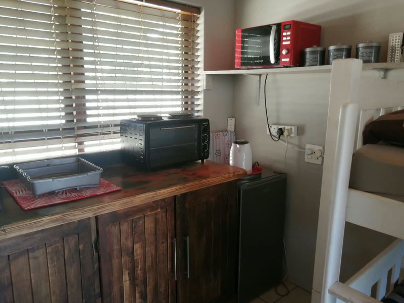 A compact kitchenette or scullery area featuring rustic wooden cabinetry, a timber countertop, and venetian blinds, providing functional prep space.