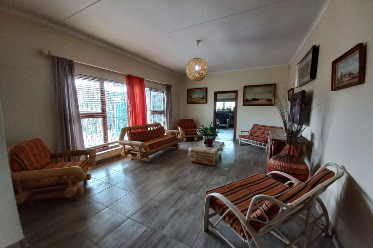 A spacious living room featuring large windows with security bars, neutral tiled flooring, and a central pendant light fixture.
