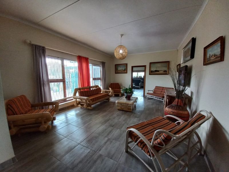 A spacious living room featuring large windows with security bars, neutral tiled flooring, and a central pendant light fixture.