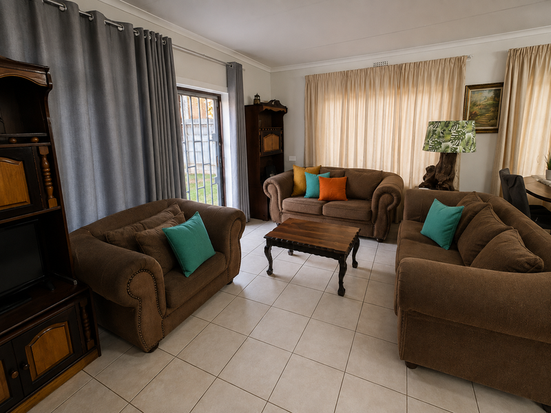 A comfortable living room featuring neutral tiled flooring, a sliding glass door providing outdoor access, and classic cove cornice detailing.