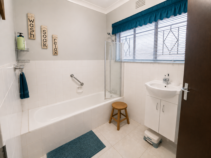 A functional bathroom featuring a bathtub with a glass screen, tiled walls, and a vanity basin with storage cabinetry.