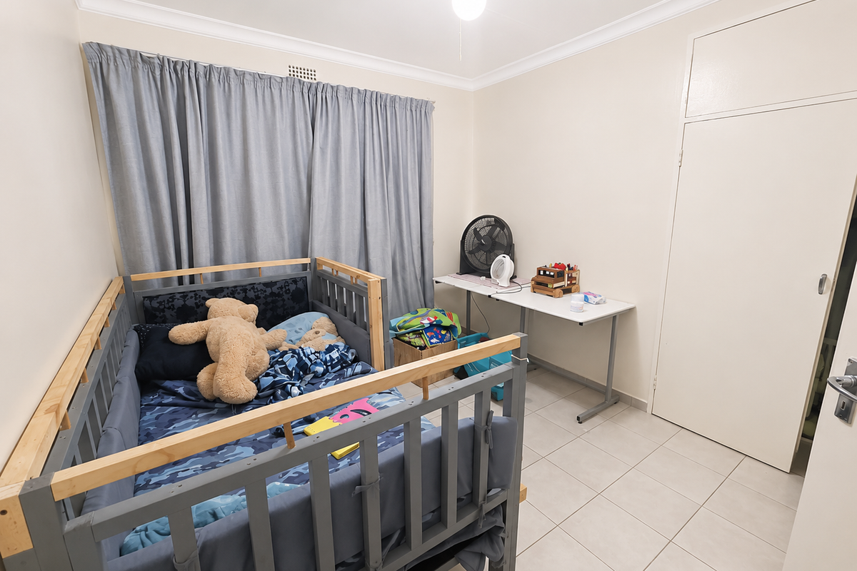 A functional bedroom featuring neutral wall tones, tiled flooring, and a built-in cupboard, providing a clean and practical space.
