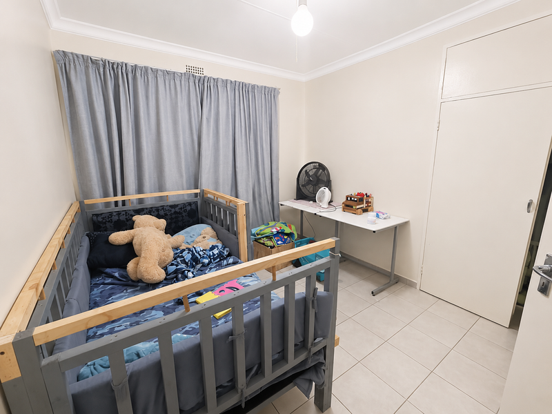 A functional bedroom featuring neutral wall tones, tiled flooring, and a built-in cupboard, providing a clean and practical space.