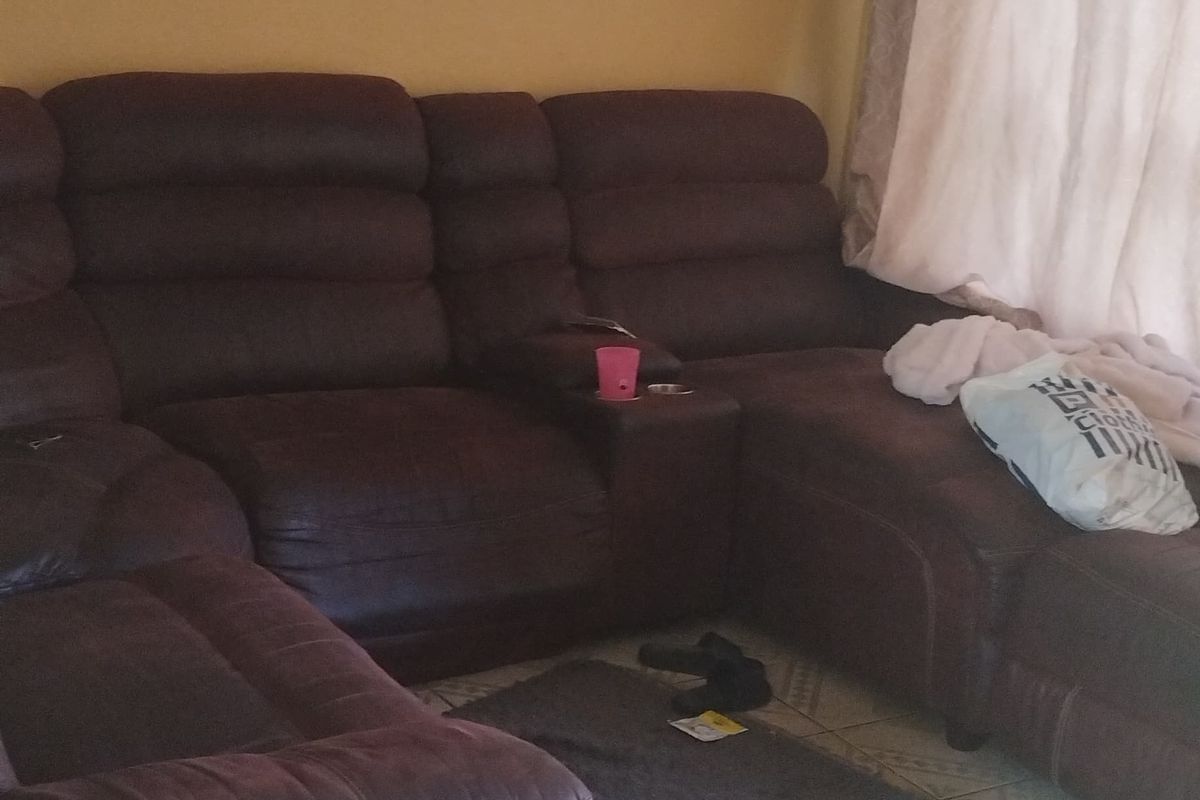 A living room area featuring tiled flooring and a textured ceiling, currently furnished with a large sectional sofa.