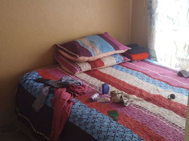 A compact bedroom featuring tiled flooring and visible water staining on the ceiling, requiring maintenance and cosmetic updates.