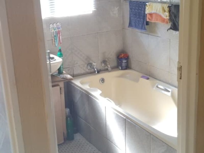 A compact bathroom featuring a built-in bathtub, tiled walls and flooring, and a vanity basin, offering a functional space ready for modernization.