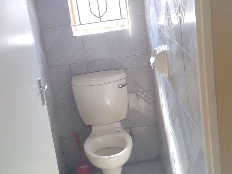 A compact, fully tiled guest toilet featuring a standard white toilet suite and a window with a security gate.