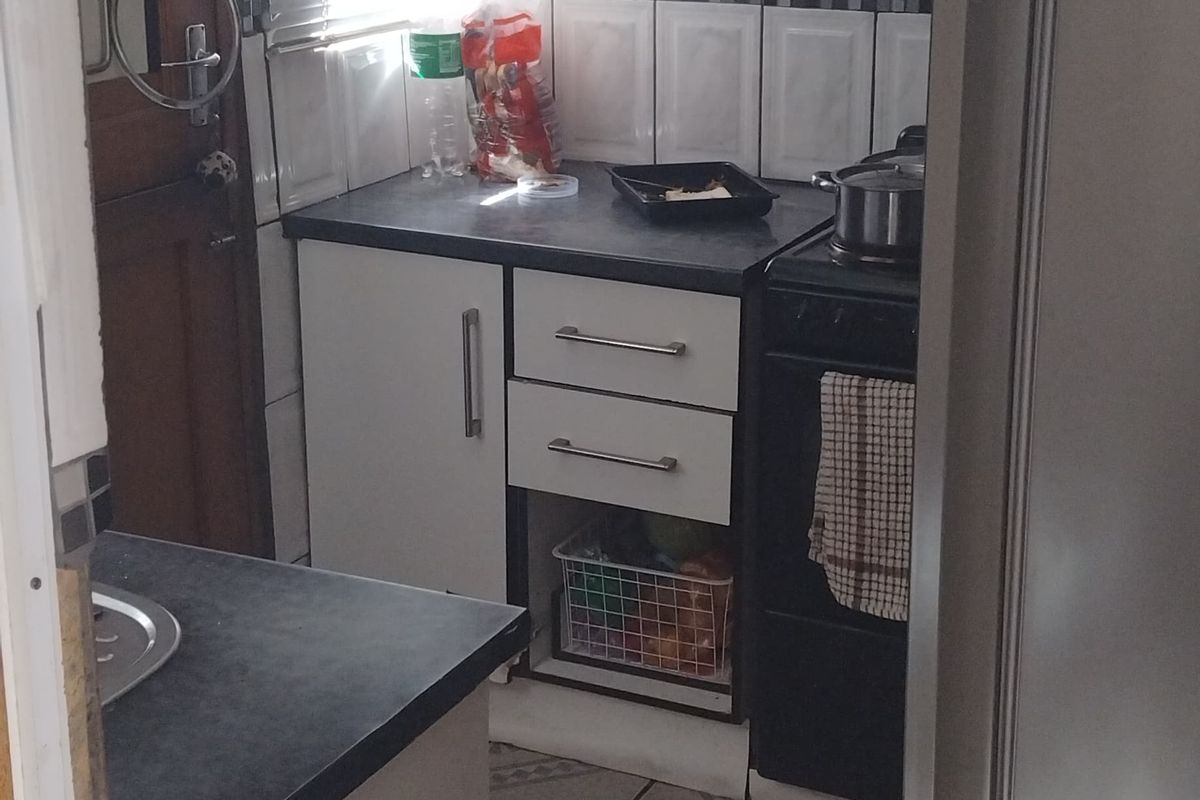 A compact kitchen featuring white cabinetry, dark laminate countertops, tiled backsplash, and ceramic flooring, equipped with a freestanding stove and extractor fan.