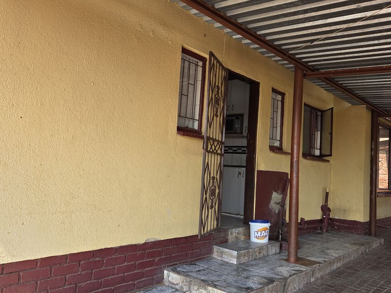 Covered patio area featuring a corrugated metal roof, metal support columns, and tiled steps leading to the main entrance.