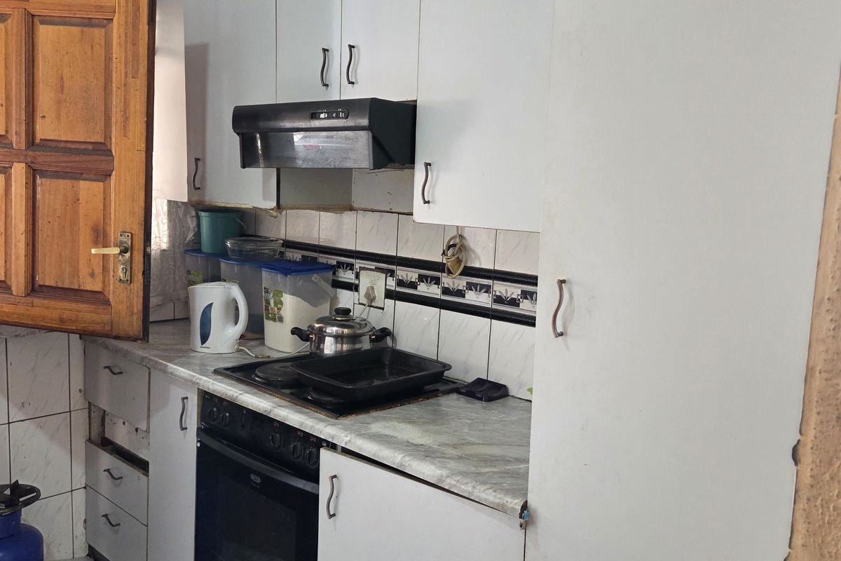 A compact kitchen featuring white built-in cabinetry, a built-in oven with hob, extractor fan, and tiled finishes, currently showing signs of wear and maintenance needs.