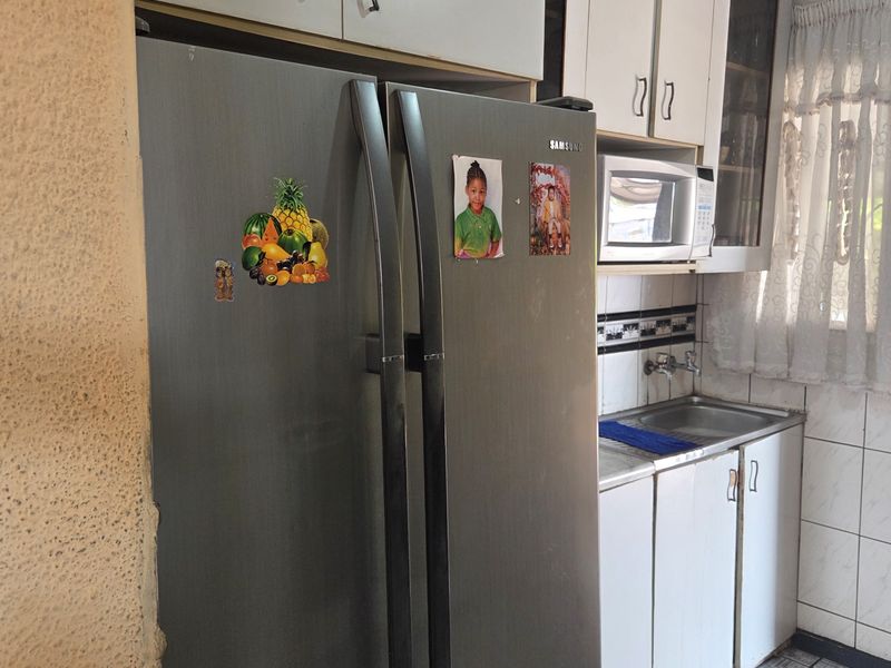 A compact kitchen area featuring white cabinetry, a stainless steel sink, tiled backsplash, and tiled flooring, showing signs of wear and dated finishes.
