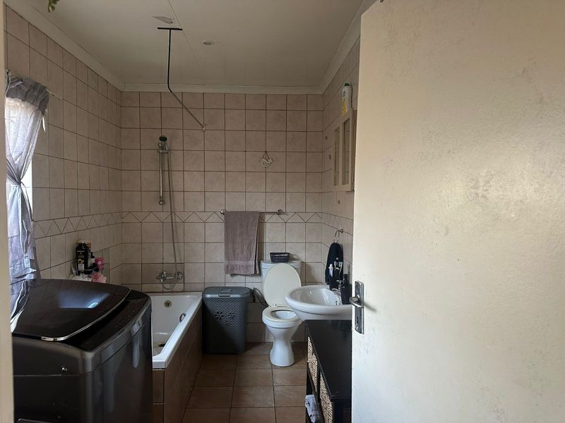 A functional bathroom featuring a bathtub with shower mixer, pedestal basin, and toilet, finished with neutral ceramic wall and floor tiling.