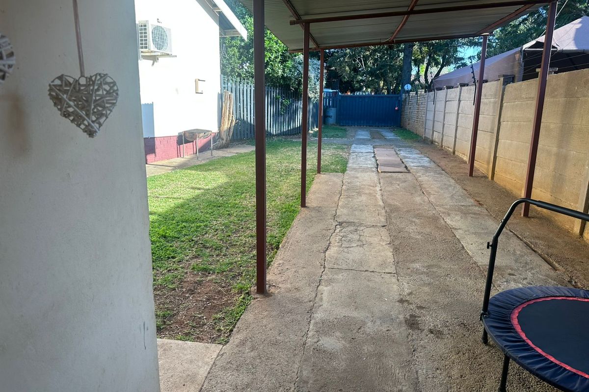 Rear exterior area featuring a covered carport, concrete driveway, perimeter walling, and a small lawn space.