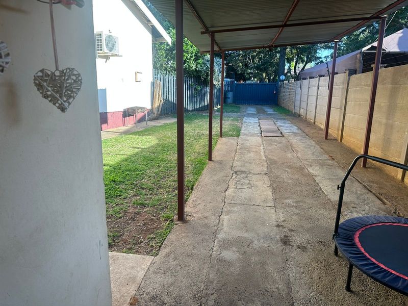 Rear exterior area featuring a covered carport, concrete driveway, perimeter walling, and a small lawn space.
